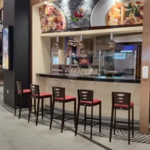 A row of dark black Eva wooden restaurant bar chairs at a polished bar counter.
